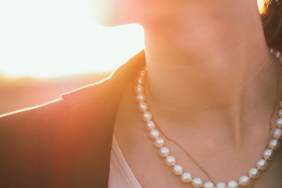 A woman wearing a pearl strand and a fine gold chain, backlit at sunset